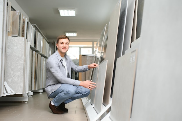 Mężczyzna architekt lub projektant wnętrz wybierający próbkę tekstury ceramicznej z tablicy próbki w studiu projektowym