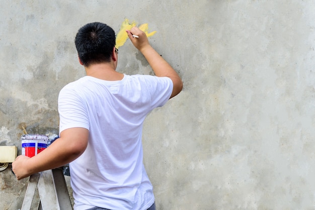Mężczyzna Azjata W Białej Koszulce Za Pomocą Pędzla Rysuje Coś Na Cementowej ścianie.