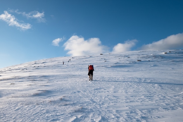 Mężczyzna backpacker wspinaczki górskiej na śnieżnym wzgórzu z błękitnym niebem na Lofotach, Norwegia