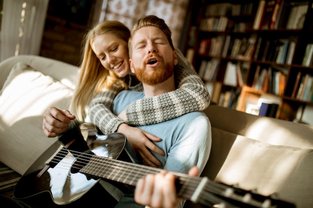 Zdjęcie mężczyzna bawić się gitarę akustyczną na kanapie