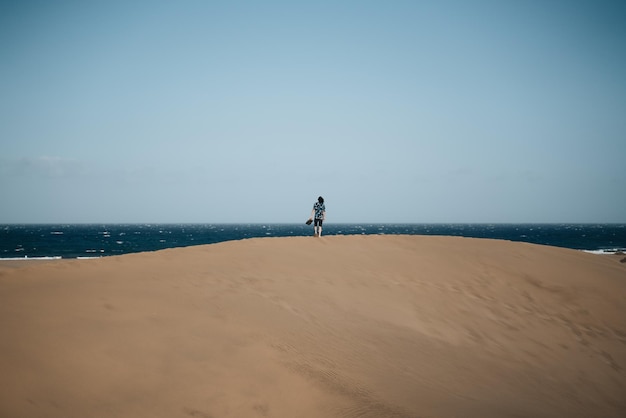Mężczyzna bez tenisówek spacerujący po środku wydmy i kontemplujący morze