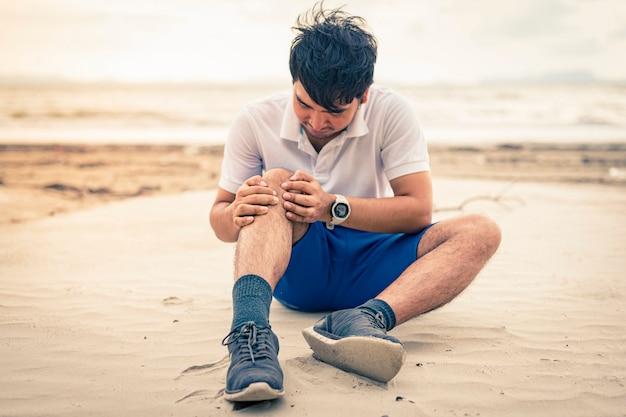 Mężczyzna biegacz trzyma jego kolano w bólu na plażowym tle