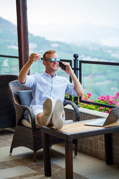Mężczyzna biznesmen pracuje na laptopie na wakacjach z pięknym widokiem na panoramę. Skuteczny menedżer pije kawę i rozmawia przez telefon z kawą podczas podróży