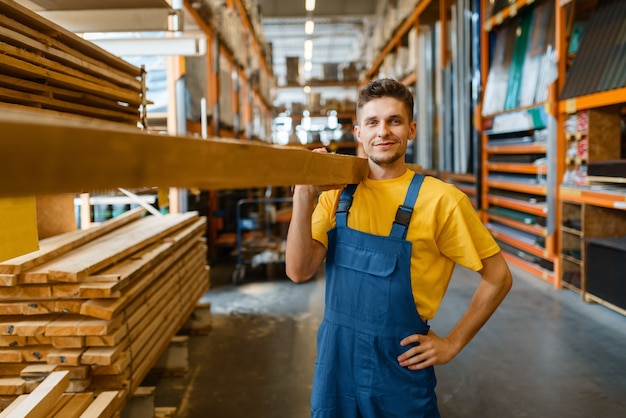Mężczyzna budowniczy trzyma drewniane deski w sklepie z narzędziami. Klient patrzy na towary w sklepie dla majsterkowiczów