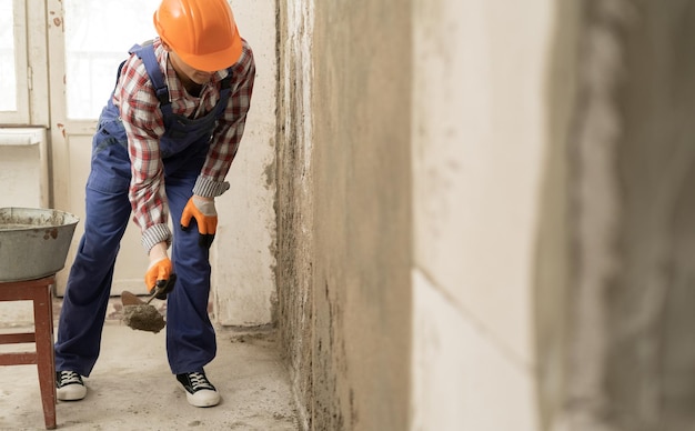 Mężczyzna budowniczy, tynker używający trowel do tynkowania ścian cementowych w budownictwie domowym, pracach budowlanych i naprawach