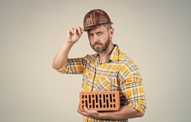 Mężczyzna buduje dom dojrzały budowniczy w koszuli nieogolony mężczyzna na budowie przystojny pracownik budowlany w kask dzień pracy facet nosić hełm ochronny trzymać cegła inżynier w pracy mężczyzna styl życia