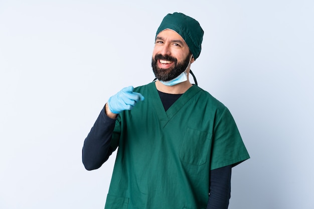 Mężczyzna chirurg w zielonym mundurze na ścianie zaskoczony i wskazując