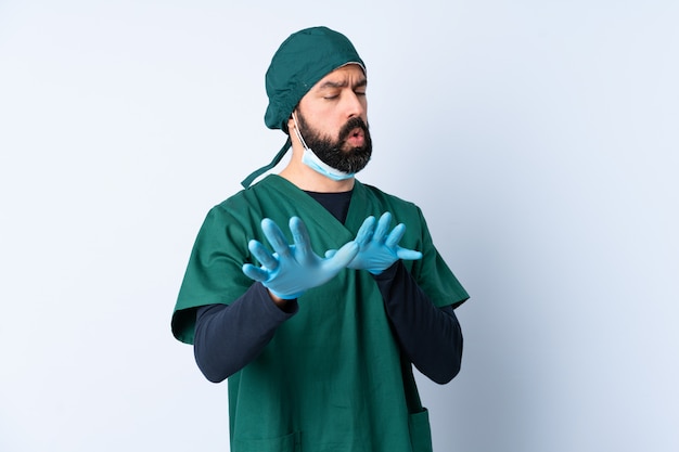 Mężczyzna chirurg w zielonym mundurze ponad izolowane ściany nerwowe ręce rozciągające się do przodu