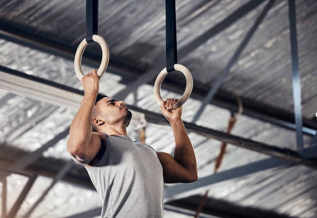 Mężczyzna ćwiczący fitness w siłowni gimnastycznej podczas treningu podciągania lub ćwiczeń na pierścieniach Młody sportowiec lub gimnastyk o silnym nastawieniu i rozpocznij trening w celu poprawy mięśni lub cardio w klubie sportowym