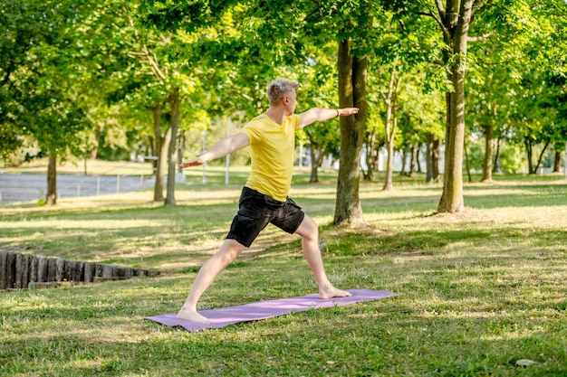 Mężczyzna ćwiczący jogę stojąc na macie na świeżym powietrzu w lecie facet ćwiczący pilates w celu rozciągania