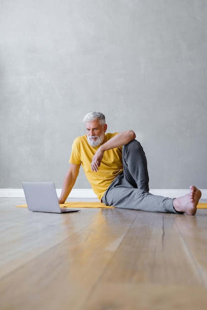 Mężczyzna ćwiczy jogę i fitness na siłowni z trenerem online z laptopa starszy męski trener sportowy