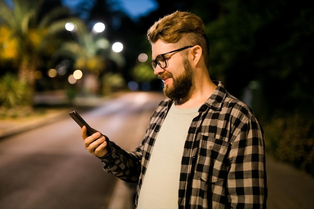 Mężczyzna Czeka Na Taksówkę, Korzystając Z Aplikacji Transportowej Na Nocne Technologie Uliczne I Koncepcję Miasta