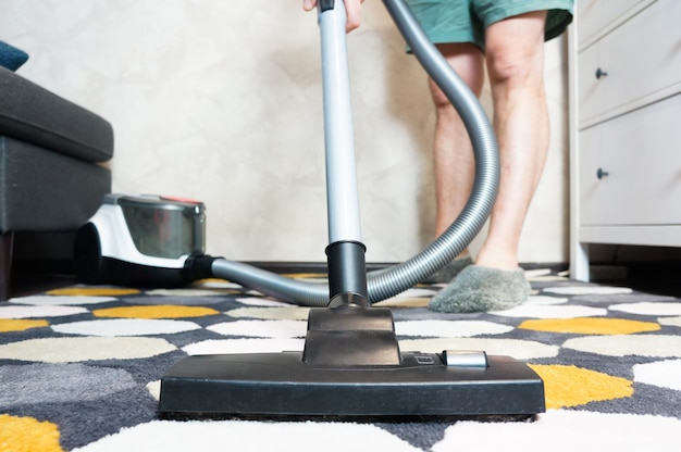 Mężczyzna czyści dywan w domu odkurzaczem sprzątając dom