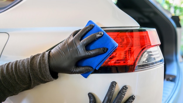 Mężczyzna czyści samochód ściereczką z mikrofibry. Mycie samochodu w garażu w domu.