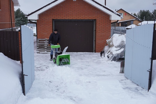 Mężczyzna czyści śnieg w zimie na dziedzińcu domu mężczyzna myje śnieg dmuchawką śnieżną