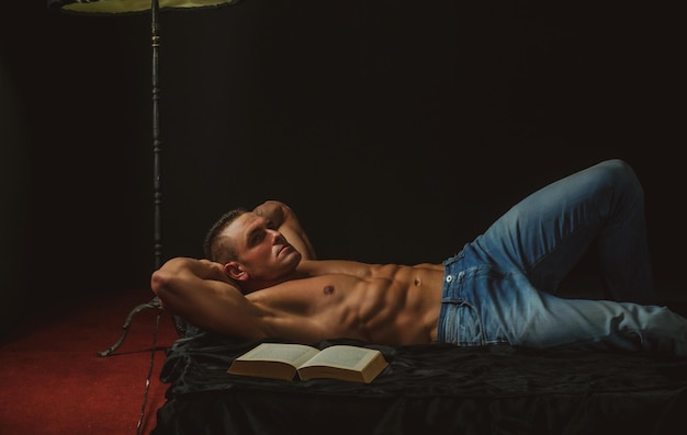 Mężczyzna czyta książkę nago w łóżku i relaksuje luksusową atmosferę seks i relaks koncepcji