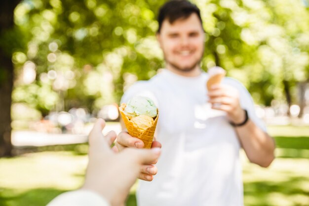 Mężczyzna dający lody w gorący słoneczny dzień w miejskim parku z punktu widzenia pierwszej osoby wyciąga rękę