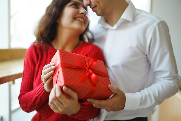 Mężczyzna daje swojej kobiecie pudełko z czerwoną wstążką Kochająca się para przytula się i świętuje Walentynki