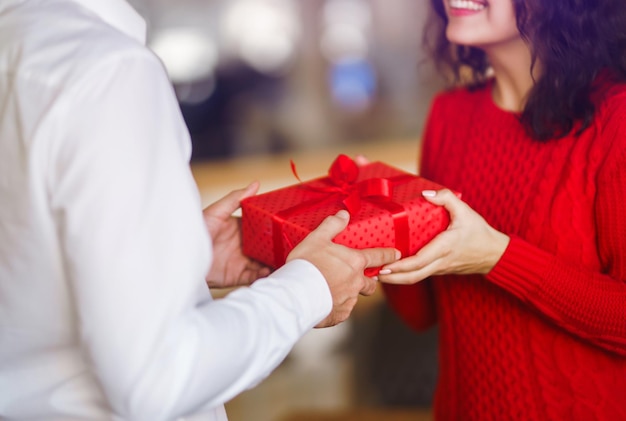 Mężczyzna daje swojej kobiecie pudełko z czerwoną wstążką Ręce mężczyzny dają niespodziankę dla dziewczyny