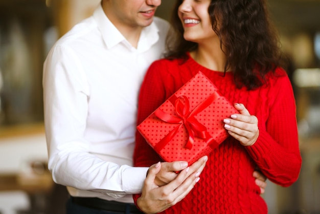 Mężczyzna daje swojej kobiecie pudełko z czerwoną wstążką Ręce mężczyzny dają niespodziankę dla dziewczyny