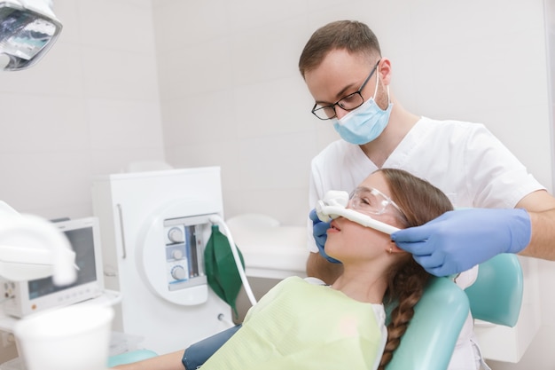 Mężczyzna dentysta nakłada inhalacyjną maskę uspokajającą na młodą dziewczynę na fotelu dentystycznym, miejsce