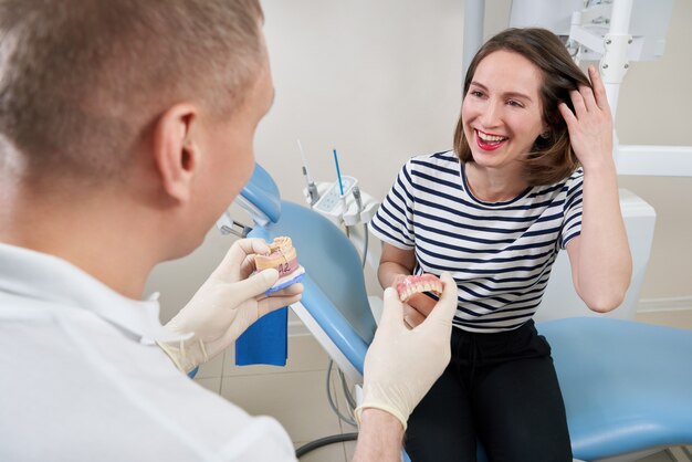 Mężczyzna dentysta pokazujący pacjentce implant dentystyczny