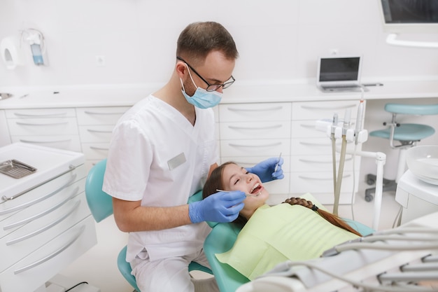 Mężczyzna dentysta pracuje w swojej klinice, badając zęby młodej dziewczyny