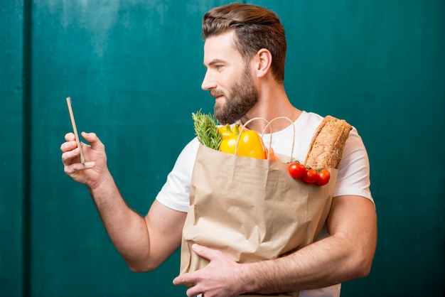 Mężczyzna Dokonujący Zakupów Online Za Pomocą Smartfona Trzymającego Papierową Torbę Pełną Zdrowej żywności Na Zielonym Tle