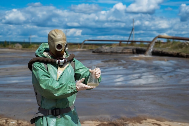 Mężczyzna ekolog w zielonym kombinezonie ochronnym i masce gazowej pobiera próbkę wody w zanieczyszczonym jeziorze do badań Produkcja odpadów Naukowiec przeprowadzający badania toksykologiczne odpadów toksycznych