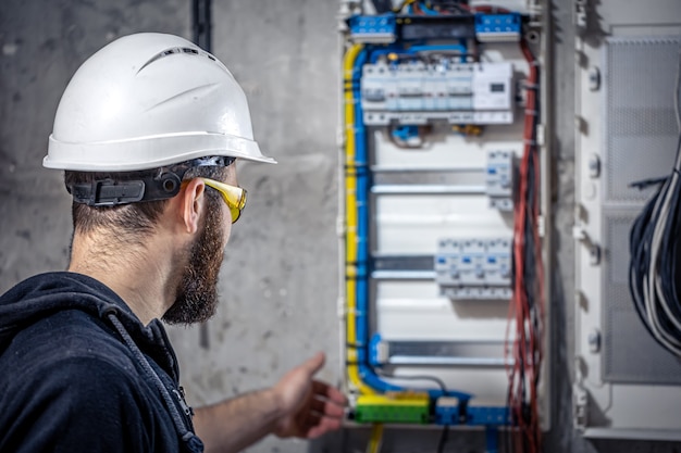 Mężczyzna elektryk w kasie na niewyraźne tło tablicy rozdzielczej.