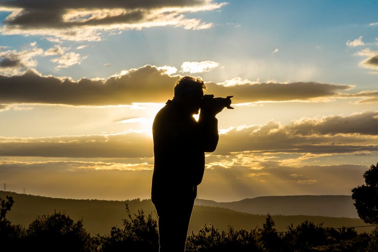 Mężczyzna fotograf fotografujący zachód słońca w dzień z chmurami.