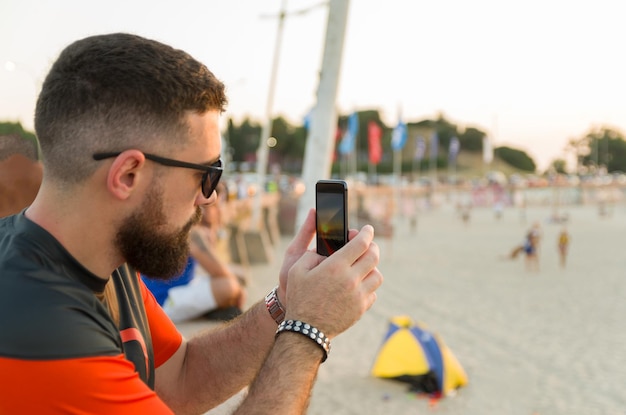 Mężczyzna fotografujący smartfonem zachód słońca na plaży