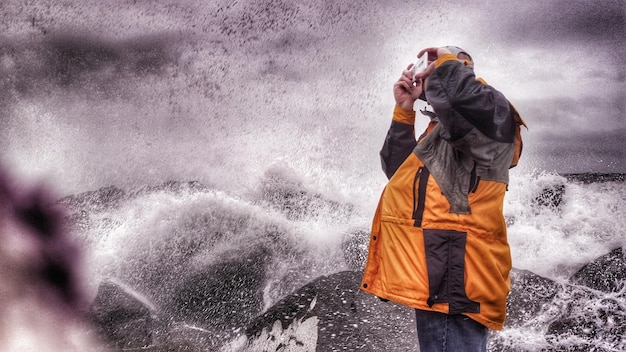 Zdjęcie mężczyzna fotografuje przez smartfon przeciwko fali rozbijającej się na brzegu przeciwko niebu