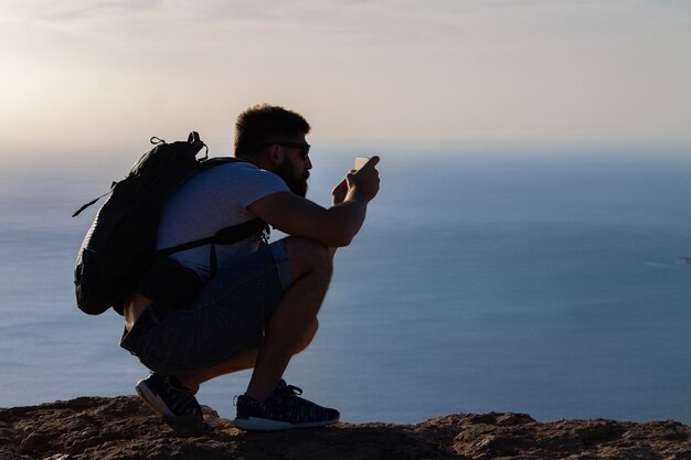 Mężczyzna fotografuje wyspę na oceanie, kucającą na krawędzi klifu. Mirador del Rio, Lanzarote, Hiszpania.