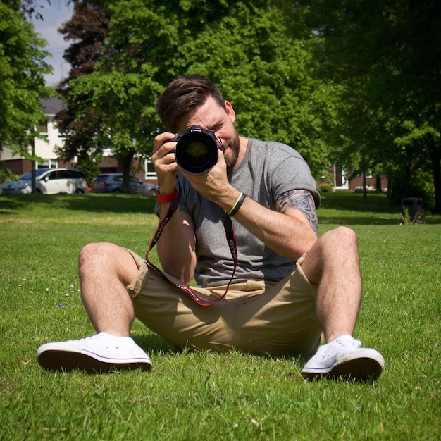 Mężczyzna fotografuje z aparatem, siedząc na trawiastym polu