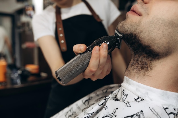 Mężczyzna golący brodę elektryczną brzytwą w zakładzie fryzjerskim