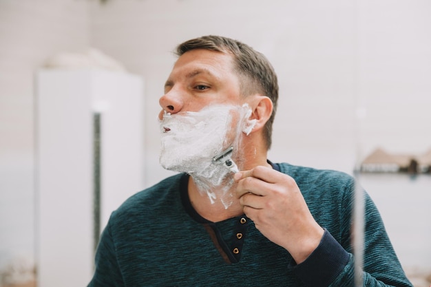 Mężczyzna goli brodę przed lustrem w swojej łazience.