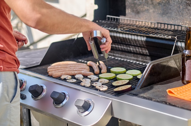 Zdjęcie mężczyzna gotujący grillowane kiełbaski i warzywa