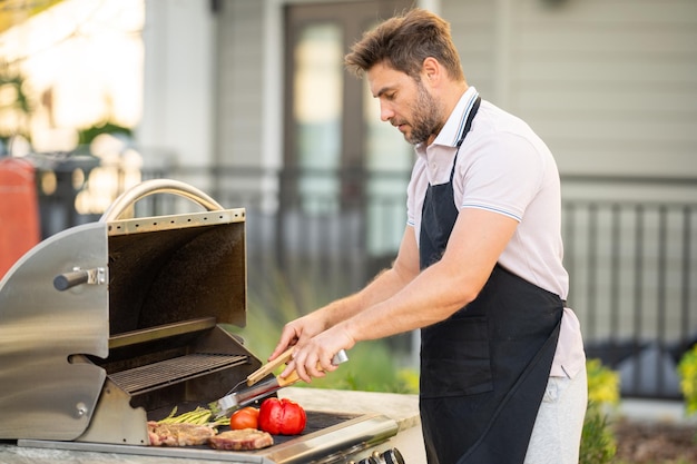 Mężczyzna gotujący mięso na grillu na podwórku domu przystojny mężczyzna przygotowujący grilla c