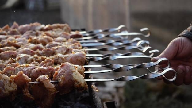 Zdjęcie mężczyzna gotuje grilla na szaszłykach na grillu węglowym na ulicy grill na świeżym powietrzu piknik w przyrodzie obraca szaszłyki z grillowanym mięsem zbliżenie