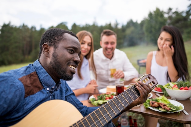 Zdjęcie mężczyzna gra na gitarze dla swoich przyjaciół przy grillu