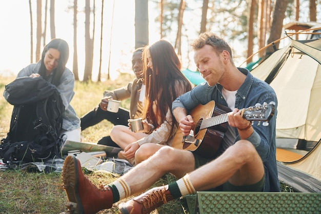 Mężczyzna gra na gitarze Grupa młodych ludzi podróżuje razem po lesie w ciągu dnia