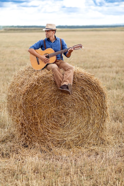 Mężczyzna gra na gitarze na stogu siana na polu