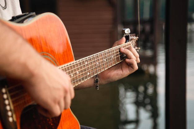 Mężczyzna gra na gitarze siedząc na drewnianym molo w pobliżu jeziora koncepcja rekreacji na świeżym powietrzu