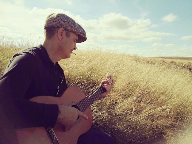 Zdjęcie mężczyzna grający na gitarze akustycznej na trawiastym polu na tle nieba