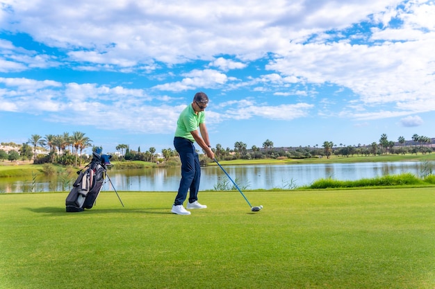 Mężczyzna grający w golfa na profesjonalnym polu golfowym Golfista uderzający piłkę kijem kierowcy obok jeziora