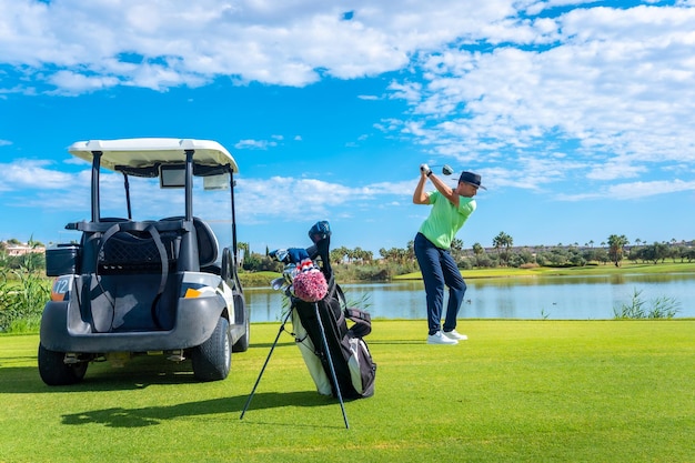 Mężczyzna grający w golfa w klubie golfowym nad jeziorem uderzający piłkę obok samochodu buggy