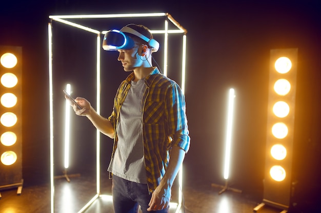 Mężczyzna grający w wirtualnej rzeczywistości zestaw słuchawkowy i gamepad w świecącej kostce. Ciemne wnętrze klubu, technologia VR, wizja 3D