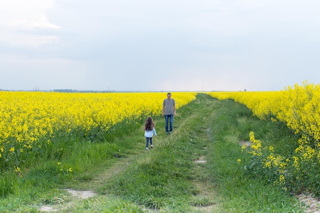 Mężczyzna i dziewczyna idą ścieżką w polu żółtych kwiatów.