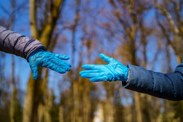 Mężczyzna i kobieta ręce w rękawiczkach medycznych rozciągają się do siebie. Park z wysokimi drzewami rozmazane tło. Selektywne skupienie. Epidemia koronowirusa. COVID-19 i identyfikacja koronawirusa. Pandemia